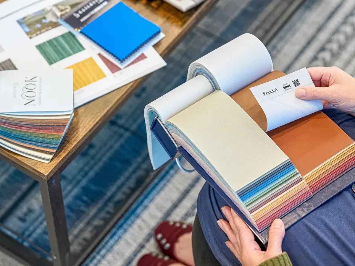 A colour swatch book being turned to a colour, with fabric samples spread across a table