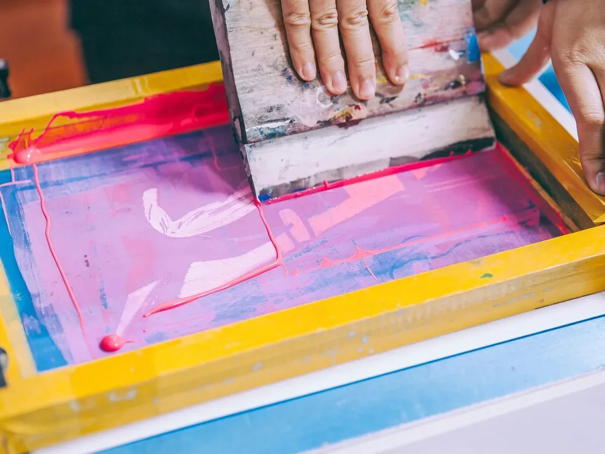 Pink ink being pulled across a silkscreen with a squeegee during a print run
