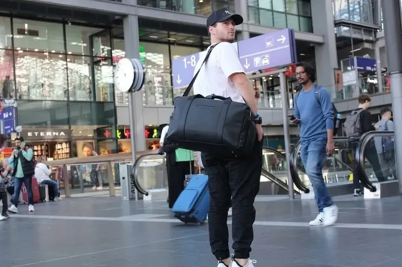 Black travel duffle carried through a station concourse