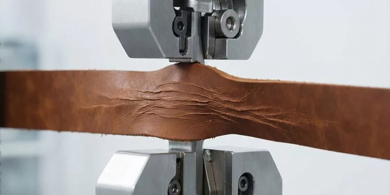 Tensile strength testing machine clamping and pulling a strip of waxed leather in a quality control laboratory.