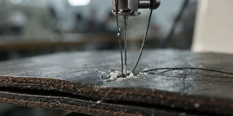 Industrial sewing machine stitching thick waxed leather with bonded nylon thread, showing slight wax residue.