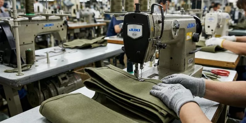 Close-up of a Juki 1541 industrial sewing machine stitching thick canvas material on a factory floor.
