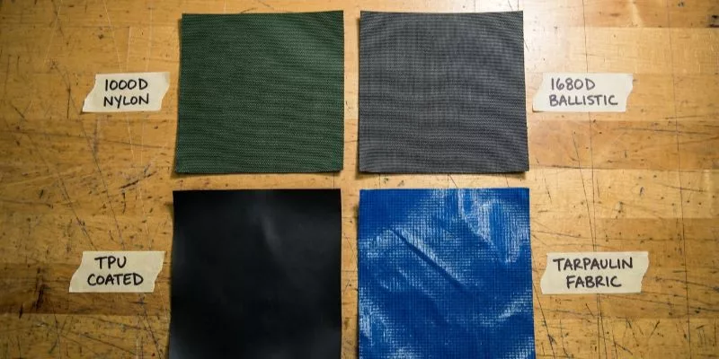 Comparison of 1000D nylon, 1680D ballistic, TPU, and Tarpaulin fabric swatches on a factory table