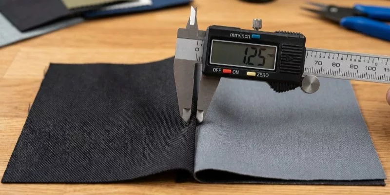 3. Caliper measuring thickness of two different gym bag fabric samples.