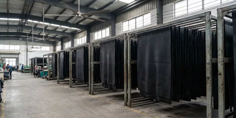 Fogli di gomma neoprene appesi su scaffalature industriali per il processo di vulcanizzazione dei VOC