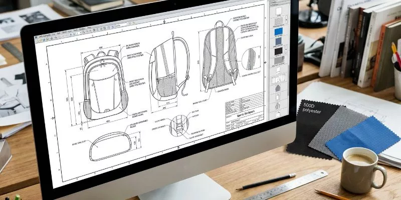 Detailed tech pack blueprint for a sports backpack shown on a monitor next to real fabric swatches.