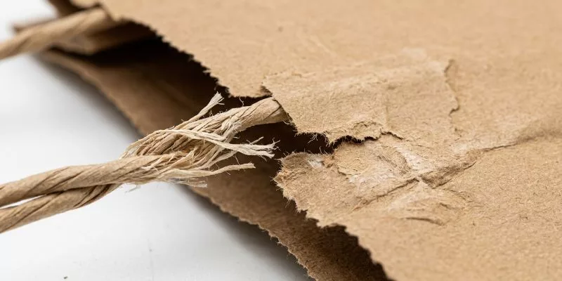 Detailed view of tear propagation and fiber failure at the handle attachment point of a heavy-duty paper bag.