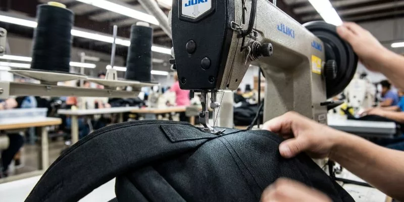 Juki industrial sewing machine stitching a backpack reinforcement point during bulk assembly