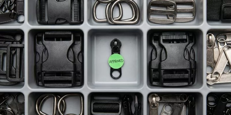 Tray of various hardware trims and zipper pulls with one specific zipper marked as approved.