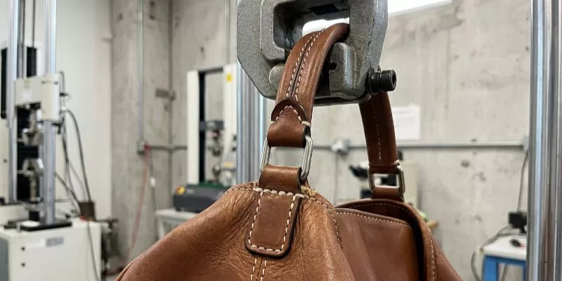 Poignée de sac à main en cuir soumise à des tests de tension et de résistance des coutures extrêmes dans un laboratoire d'usine.